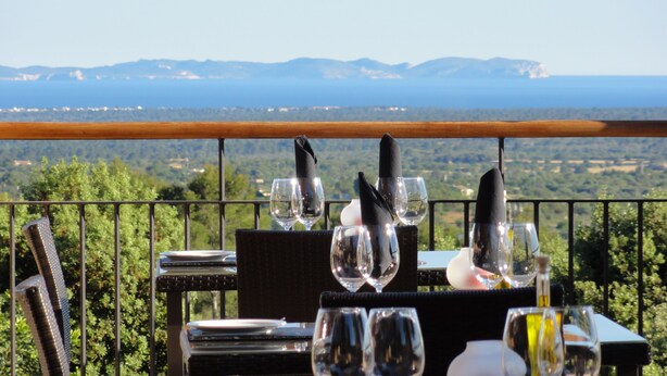 A table set for dining with a scenic view of mountains and a body of water in the background. - Finca Son Samà (Llucmajor)