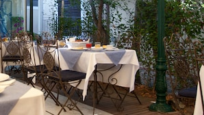 Un espace de restauration en plein air avec des tables préparées pour le petit-déjeuner, entouré de chaises en métal et d’une clôture décorative.