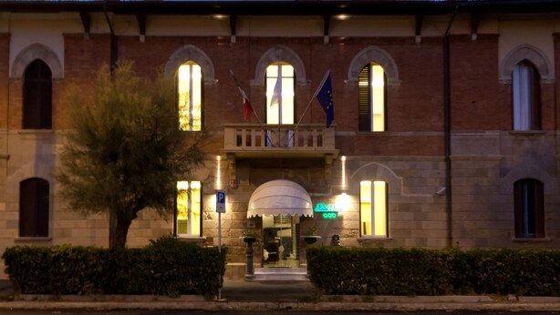 Un bâtiment historique doté de fenêtres en arc de cercle, d’une entrée centrale surmontée d’un auvent et de drapeaux.