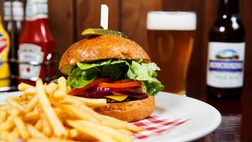 A burger with fries on a plate, a glass of beer, and condiments in the background.