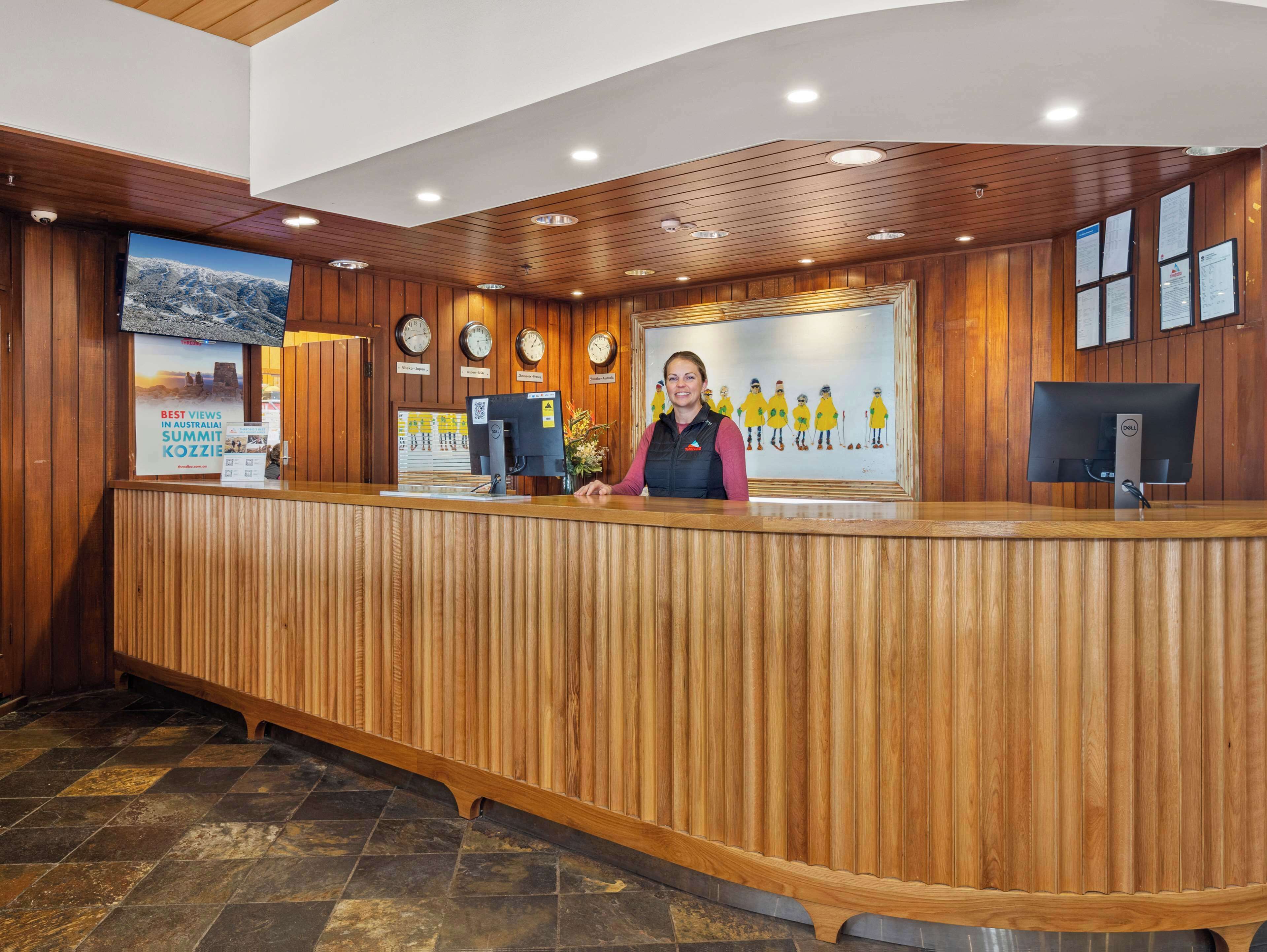 A reception desk with a wooden finish, a digital clock, and a framed painting of skiers.