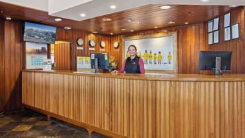 A reception desk with a wooden finish, a digital clock, and a framed painting of skiers.