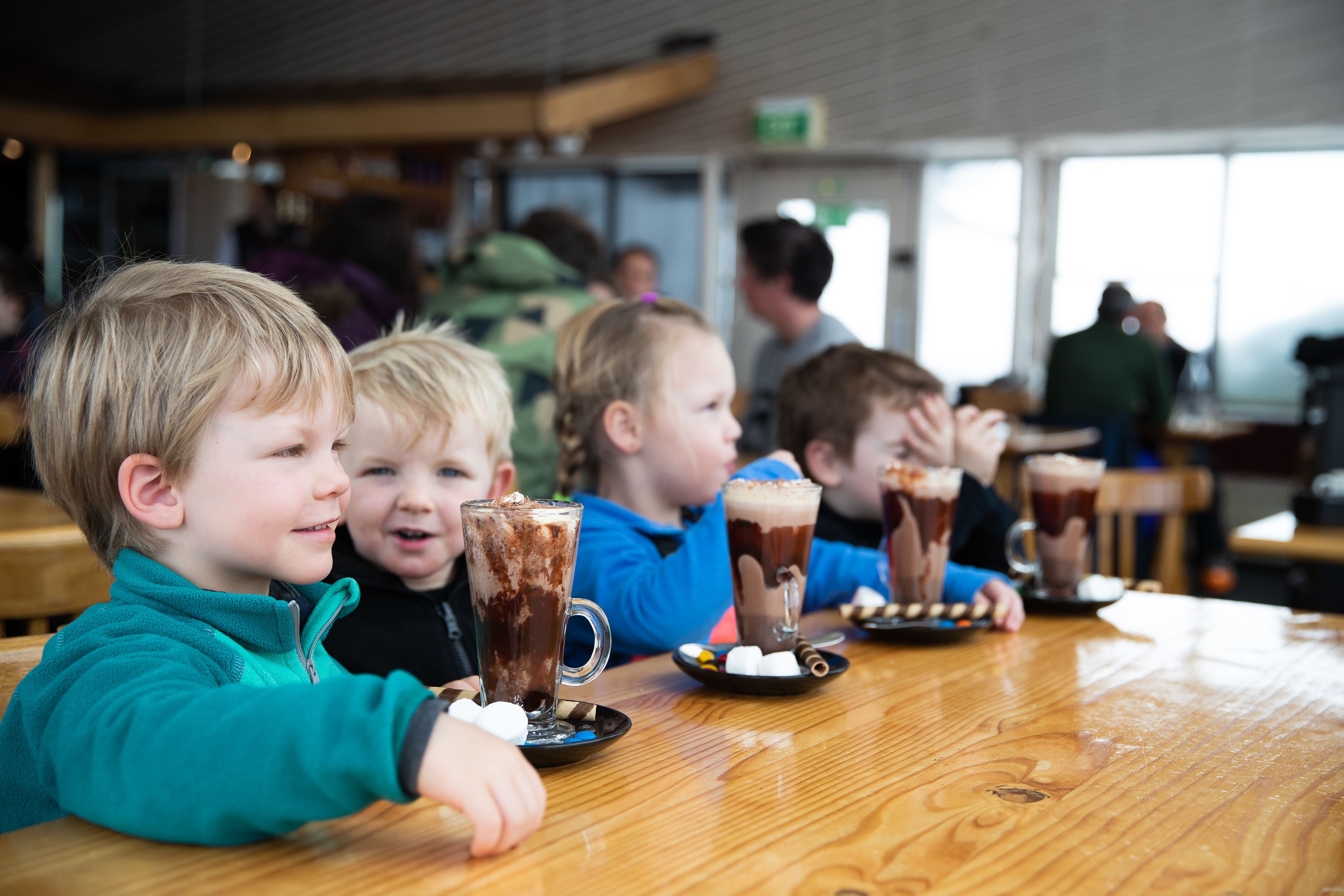 A group of children seated at a wooden table with drinks and marshmallows.