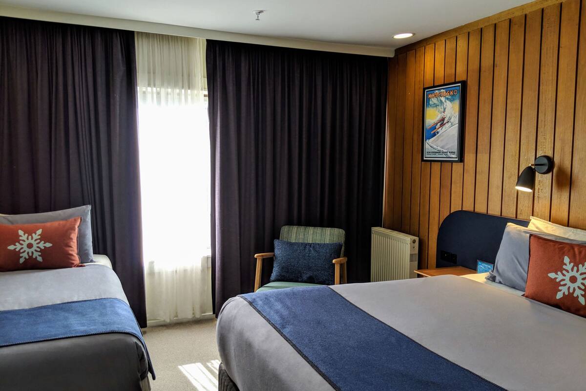 A hotel room with two beds, a wooden panel wall, a poster, and a radiator.