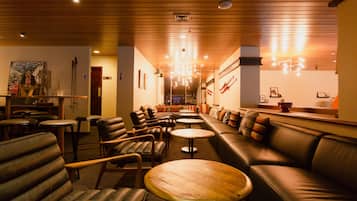 A cozy lounge area with leather sofas, wooden tables, and a bar area in the background.