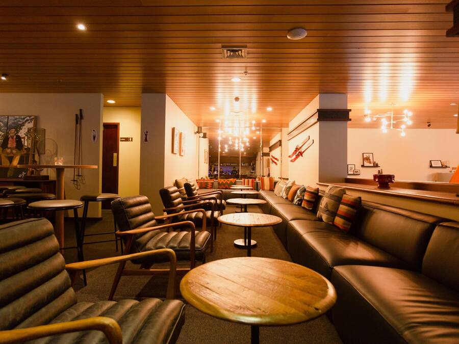 A cozy lounge area with leather sofas, wooden tables, and a bar area in the background.