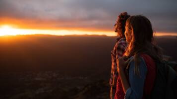 Two people standing on a hill overlooking a city at sunset.
