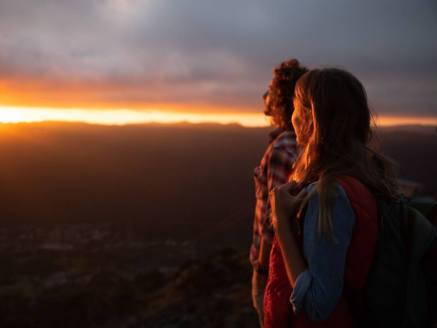Two people standing on a hill overlooking a city at sunset.
