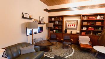 A cozy living room with a sofa, chairs, a coffee table, and a fireplace. There are shelves with books and decorative items.