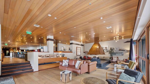 A spacious lobby with wooden flooring, a reception desk, a seating area with sofas and chairs, and a large pendant light.