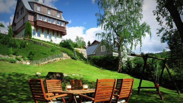 A wooden deck with outdoor furniture and a view of a large house in the background. - Pension Seidl (Spindleruv Mlyn)