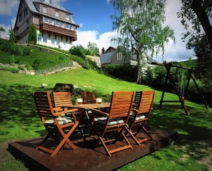 A wooden deck with outdoor furniture and a view of a large house in the background. - Pension Seidl (Spindleruv Mlyn)