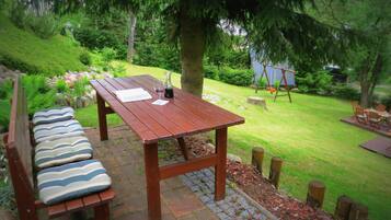 Una mesa de picnic de madera con bancos, rodeada por un jardín exuberante con un columpio al fondo.