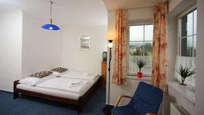 A bedroom with a bed, a blue chair, a window with curtains, and a lamp. - Pension Seidl (Spindleruv Mlyn)