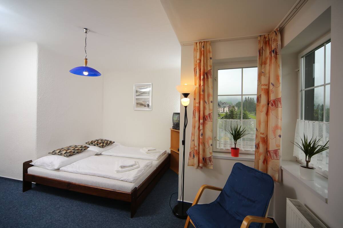 Een slaapkamer met een bed, een blauwe stoel, een raam met gordijnen en een lamp.