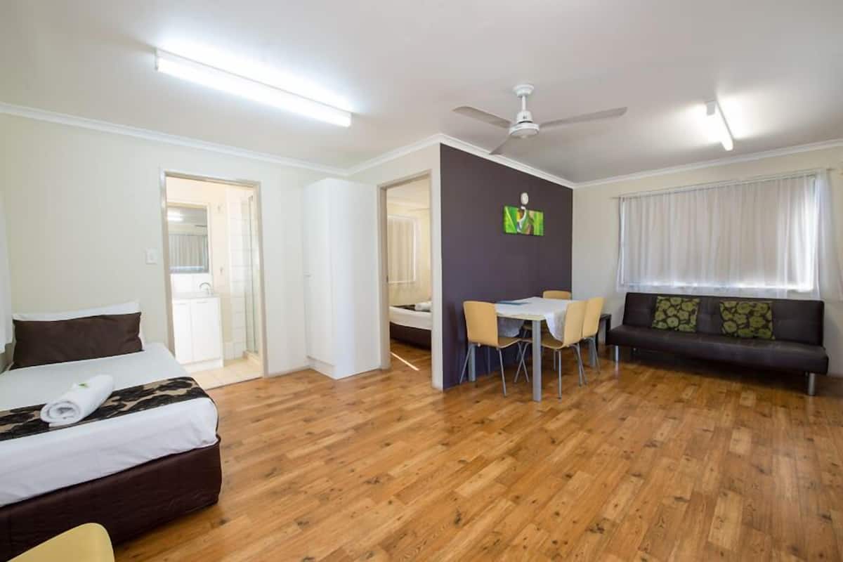 Una habitación de hotel moderna con cama, zona de comedor con sillas, sofá y ventilador de techo.