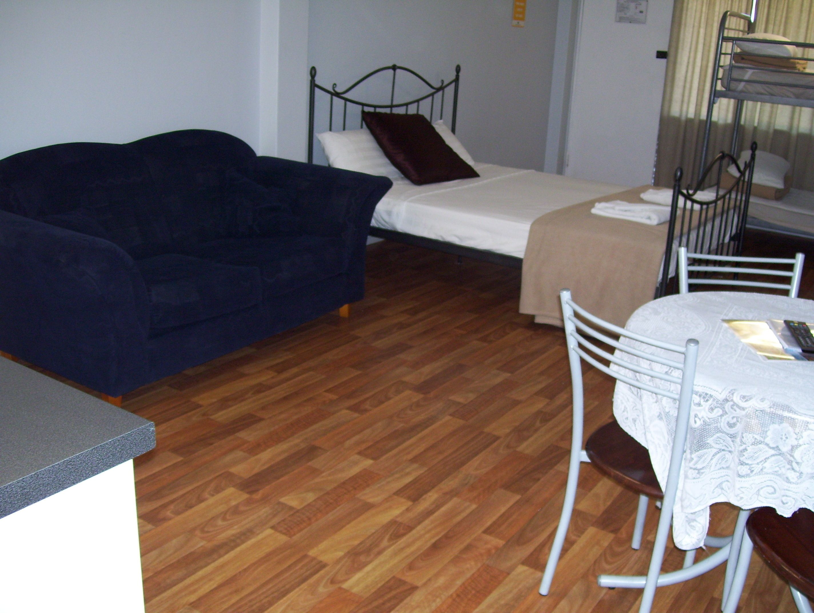 A small, furnished room with a bed, a sofa, a table, and chairs.
