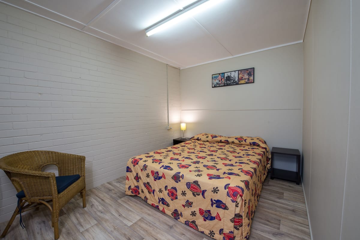 Un dormitorio con una cama, una silla, una mesita de noche y un cuadro en la pared.