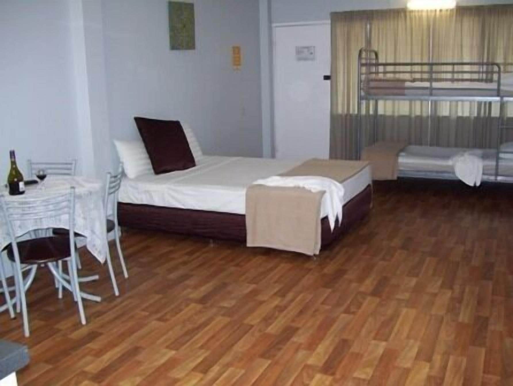 Une pièce comprenant un lit, une petite table avec des chaises, un lit superposé et un plancher en bois.