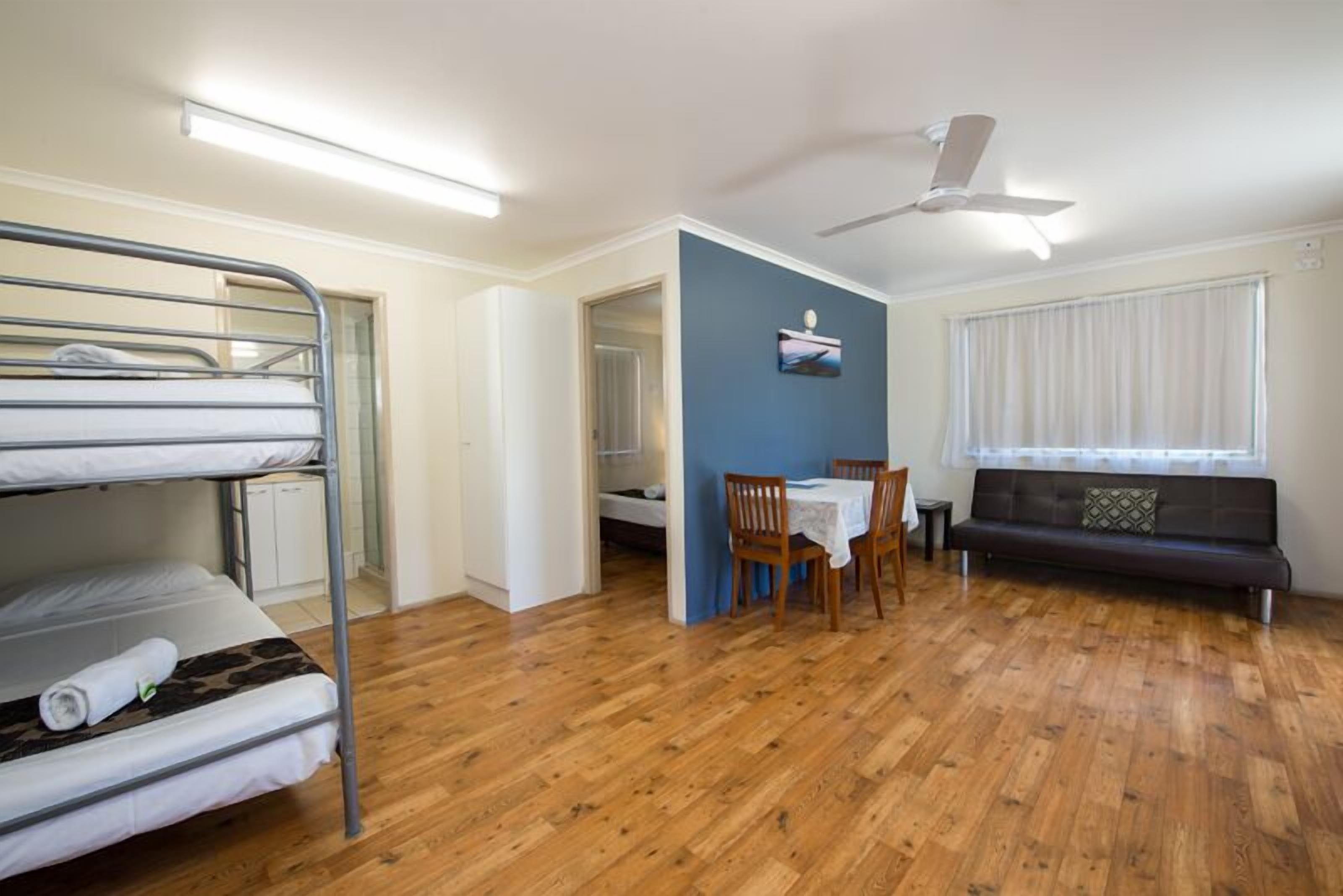 A room with bunk beds, a dining table with chairs, a sofa, and a ceiling fan.