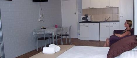 Une chambre d’hôtel de taille réduite, comprenant un lit, un petit bureau, une chaise, une télévision et une kitchenette.