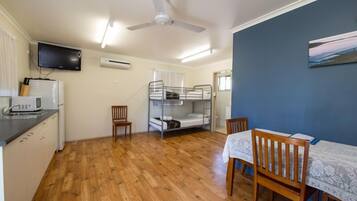 A compact room with a bunk bed, a dining table with chairs, a television mounted on the wall, and a ceiling fan.