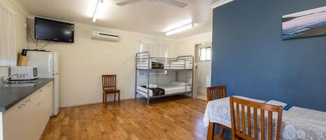 A compact room with a bunk bed, a dining table with chairs, a television mounted on the wall, and a ceiling fan.