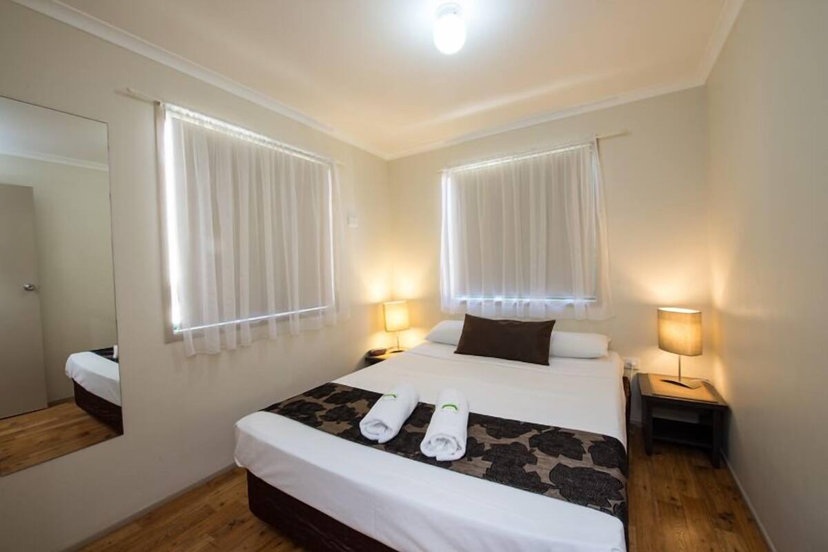 Una habitación de hotel con una cama grande, dos mesitas de noche con lámparas, un espejo y suelo de madera.