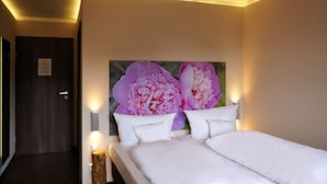 A hotel room with a bed, two wall-mounted lamps, and a large floral artwork on the wall. - Heckenrose (Ringsheim)