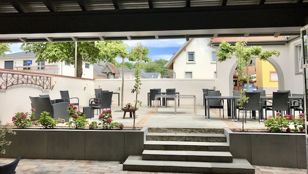 An outdoor patio area with multiple tables and chairs, a small staircase leading to an upper level, and potted plants. - Heckenrose (Ringsheim)