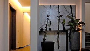 A hallway with a modern design, featuring a wall-mounted art piece with abstract branches and a large potted plant. - Heckenrose (Ringsheim)