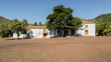 A building with a white facade and red-tiled roof, surrounded by trees and a hilly landscape.