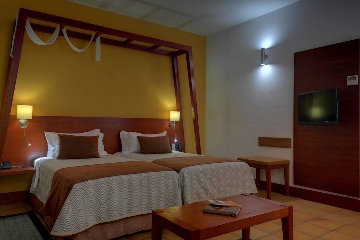 A hotel room with a large bed, two bedside tables, a small table, and a TV mounted on the wall.