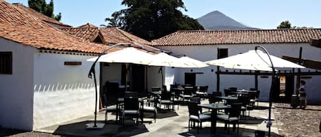 Un espace extérieur aménagé avec des tables et des chaises, des murs blancs et un toit recouvert de tuiles.