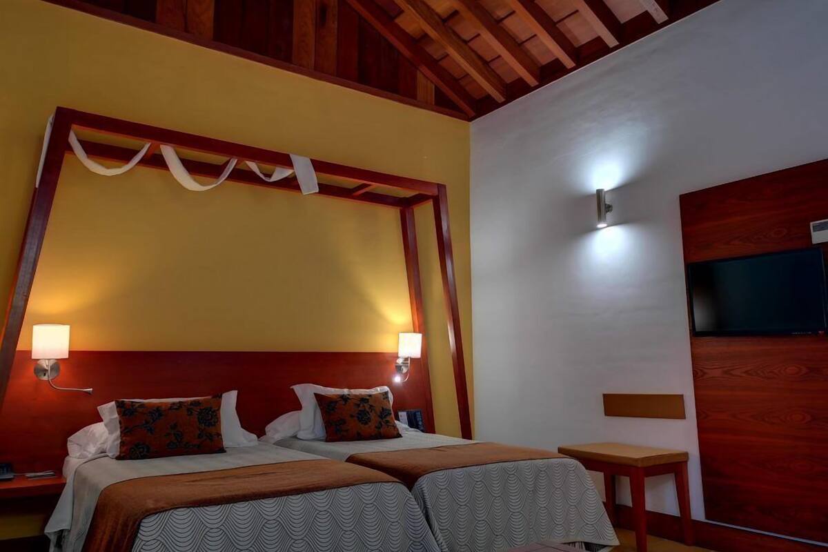 A hotel room with a wooden ceiling, a bed with two pillows, a bedside table, and a nightstand.
