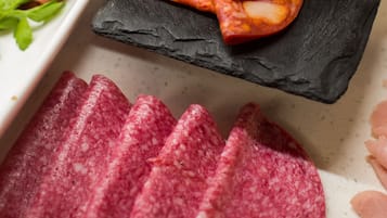 En række skiveskåret kød på en bakke, herunder salamipølse og parmaskinke, med en sort skiferplade i midten.