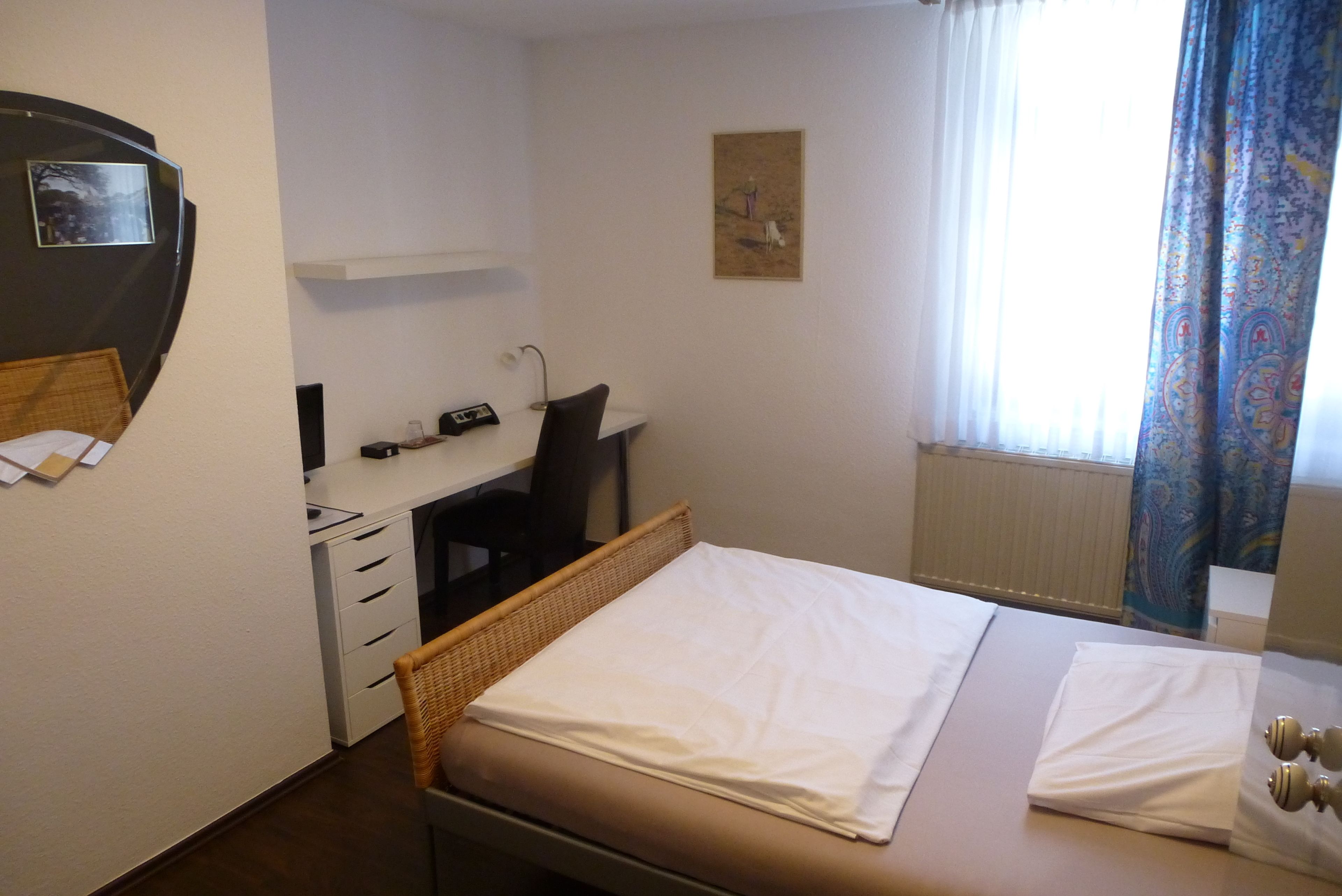 Habitación de hotel con cama, escritorio, silla, una mesita y ventana con cortinas.