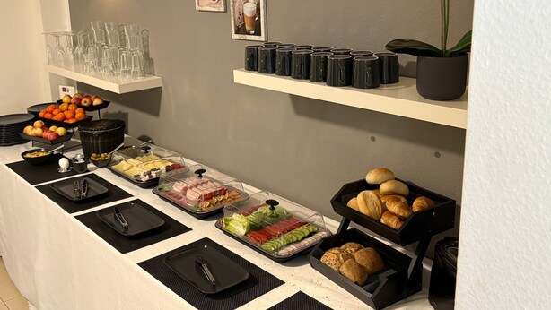 A buffet setup with various food items, clear glassware, and black mugs on shelves. - Hotel Zum Löwen (Bad Homburg v.d. Hoehe)