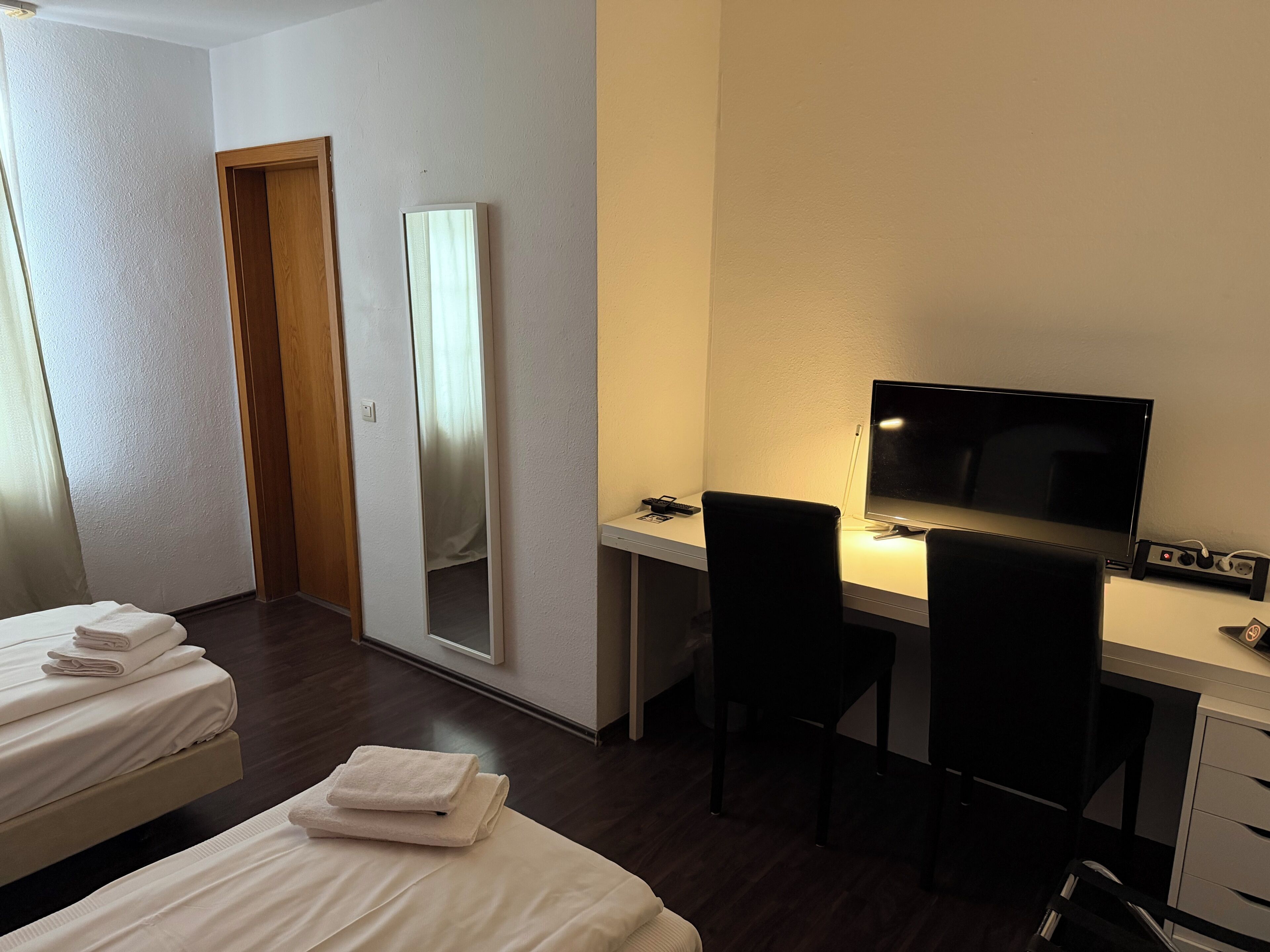 Una habitación de hotel con cama, escritorio con computadora, televisión y espejo.