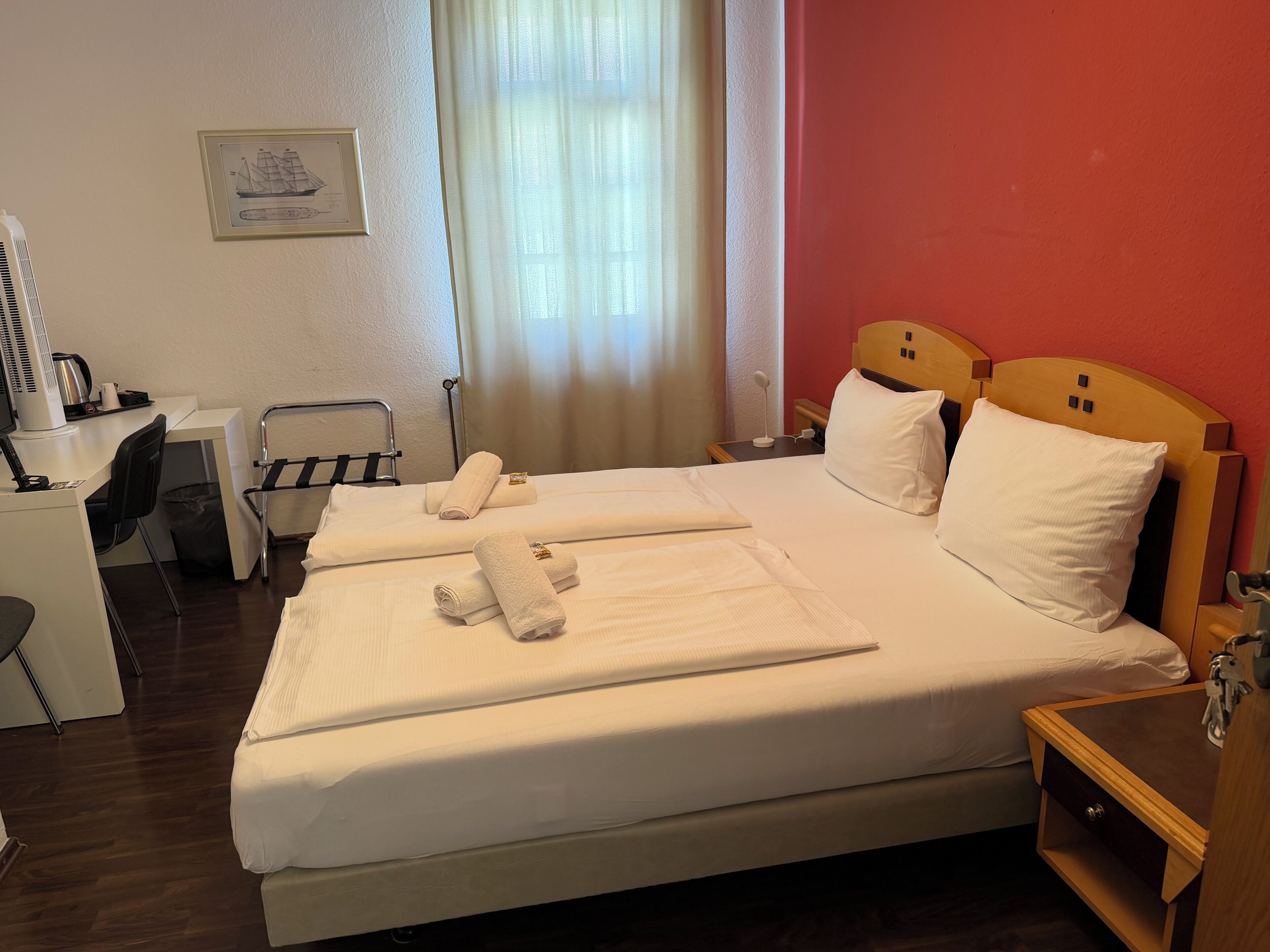 Ein Hotelzimmer mit Bett, Schreibtisch, Stuhl, Nachttisch und einem Fenster mit Vorhängen.