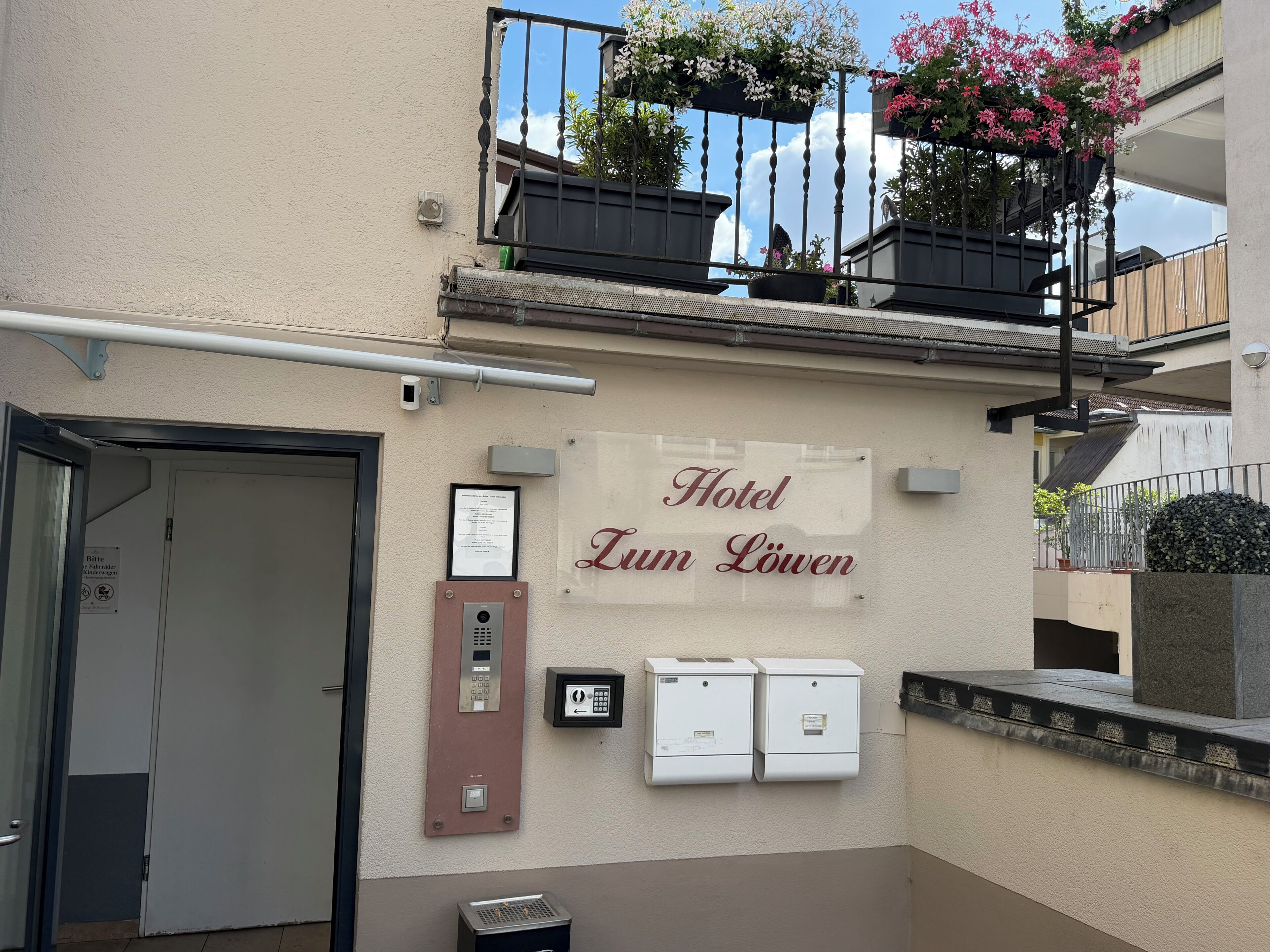 Entrada de un hotel con un cartel que dice 'Hotel Zum Löwen', una puerta, un portero automático en la pared y un buzón de seguridad.