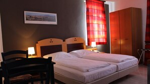 A double bed with two pillows, a nightstand with a lamp, a wooden wardrobe, and a framed picture on the wall. - Hotel Zum Löwen (Bad Homburg v.d. Hoehe)