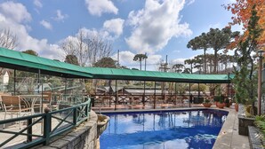 A swimming pool with a green canopy, stone steps, and outdoor seating. - Le Suisse Elegance Hotel (Campos do Jordão)
