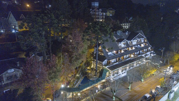 A large, multi-story building with a prominent central tower, surrounded by trees and other structures. - Le Suisse Elegance Hotel (Campos do Jordão)