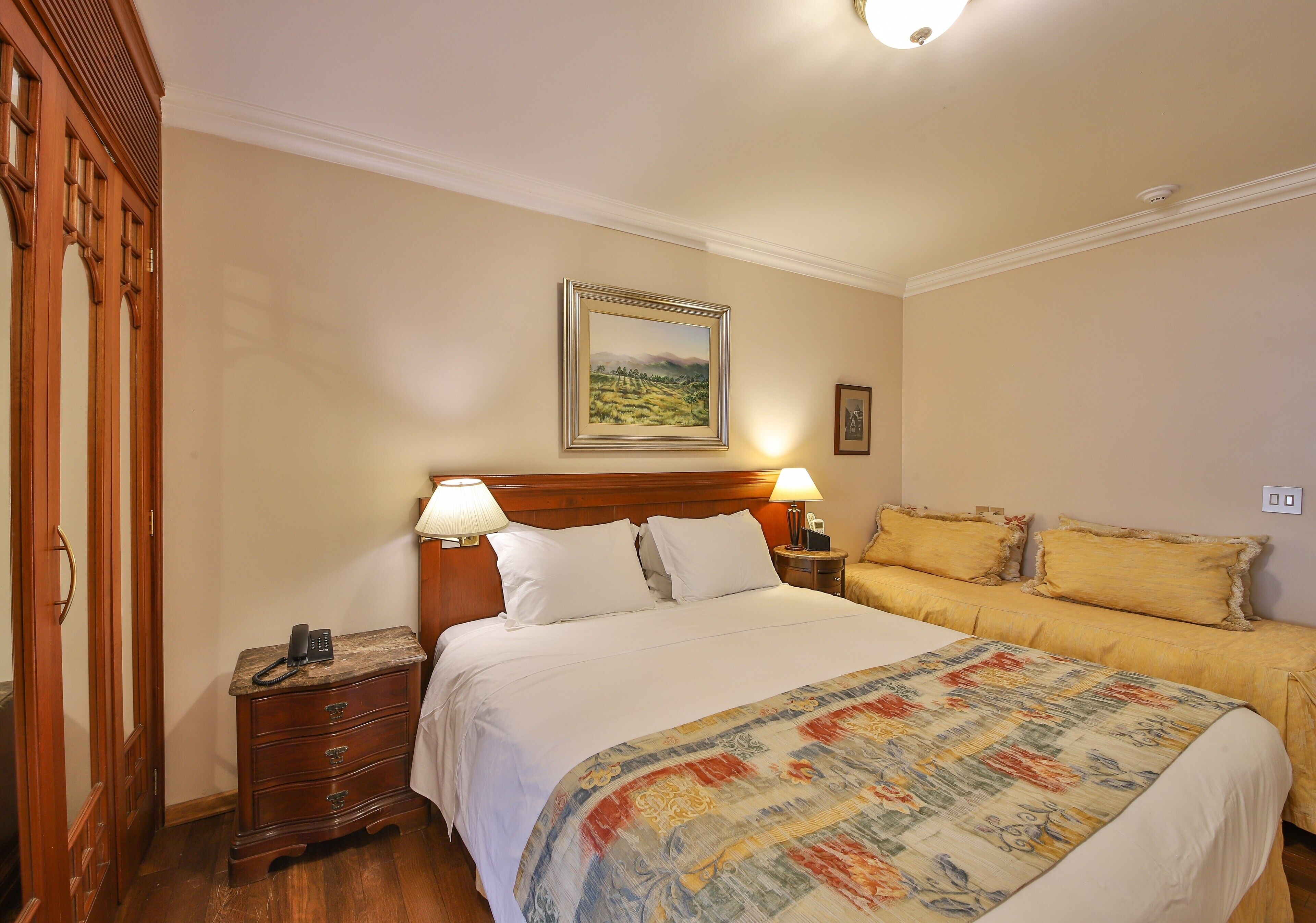 Un cuarto de hotel con una cama grande, dos mesitas de noche con lámparas, un aparador de madera y un cuadro en la pared.