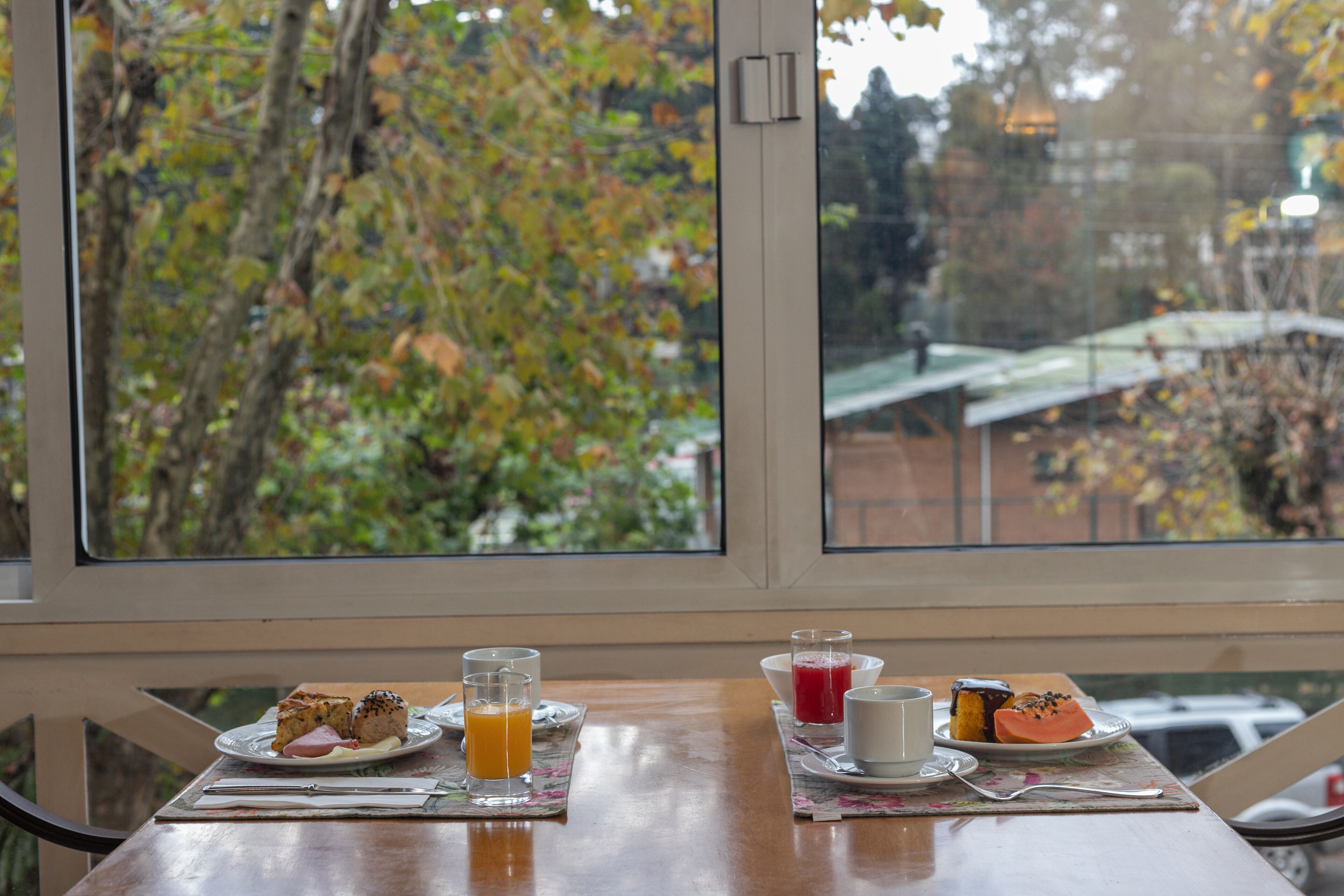 A table with breakfast items and a view of trees through a window.