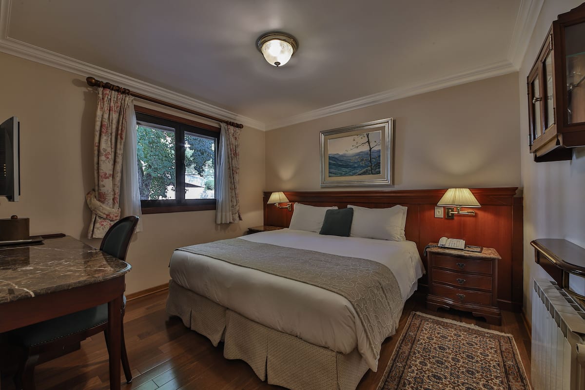 Ein Hotelzimmer mit einem großen Bett, Nachttischlampen, einem Schreibtisch und einem fensterbepflanzten Fenster mit Vorhängen.