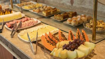 A buffet with various food items including fruits, cheeses, and pastries.