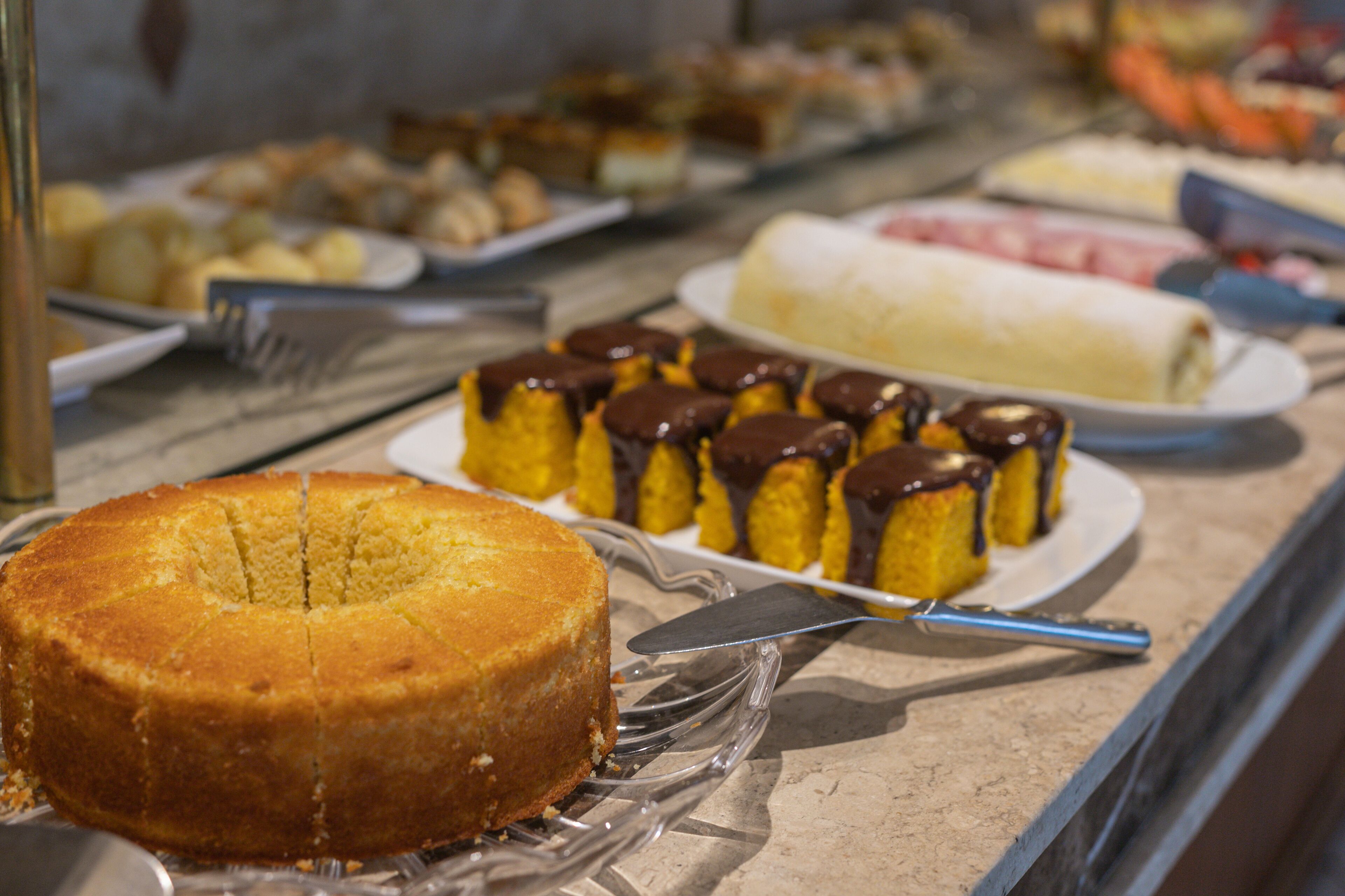 Un bufé con diversos postres, incluyendo un pastel, pastelería con cobertura de chocolate y un postre enrollado.