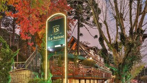 A hotel entrance with a sign, stone pathway, and autumn foliage. - Le Suisse Elegance Hotel (Campos do Jordão)